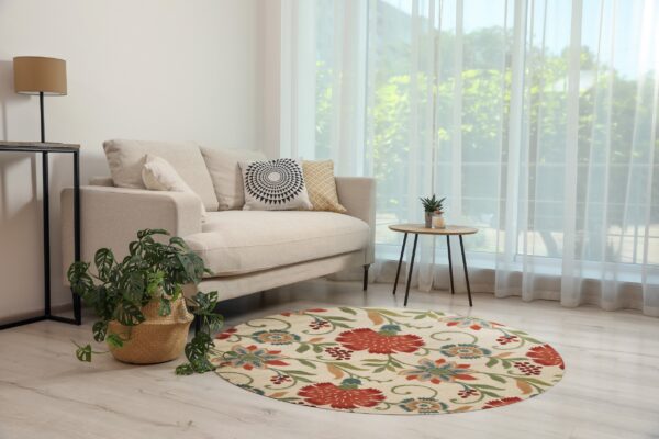Cream round rug with bold red, blue, and green floral patterns in a sunny room with a beige couch.