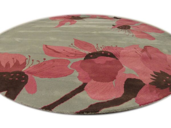 A round sage rug featuring large pink and dark brown stylized floral patterns.