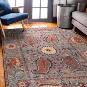 Muted blue rug with colorful paisley and floral patterns sits on wood flooring near a blue armchair.