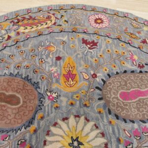 Round blue rug with carved pile, showing intricate pink, yellow, and brown floral and paisley motifs.