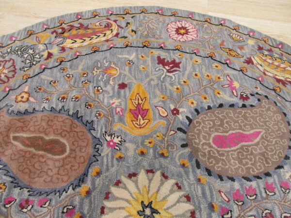 Round blue rug with carved pile, showing intricate pink, yellow, and brown floral and paisley motifs.