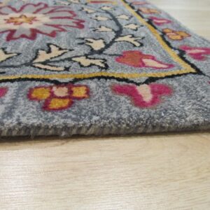 A close-up of a gray-blue floral rug with pink, yellow, and cream designs resting on light wood flooring.
