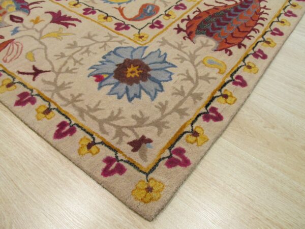Beige rug corner with detailed blue, magenta, and orange floral patterns resting on light wood flooring.