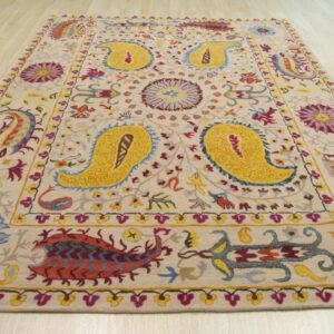 A detailed, colorful medium pile rug with yellow paisley designs rests on light wood planks.