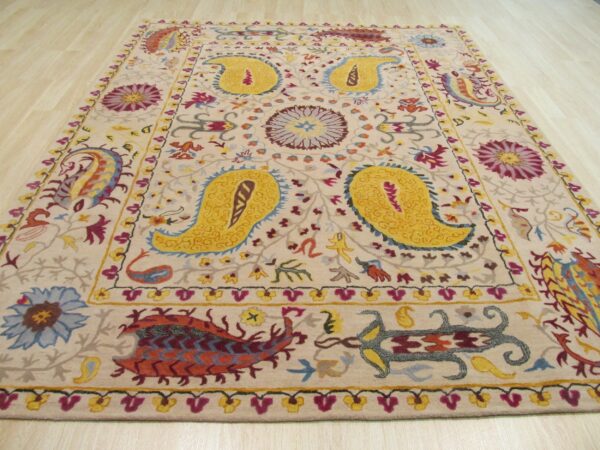 A detailed, colorful medium pile rug with yellow paisley designs rests on light wood planks.