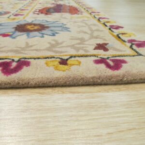 Detail shot of a cream rug featuring bright blue, yellow, and magenta floral designs on wood flooring.