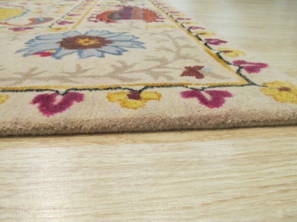 Detail shot of a cream rug featuring bright blue, yellow, and magenta floral designs on wood flooring.