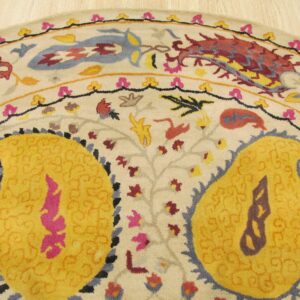 Round rug with yellow paisley and multicolored floral motifs on a cream background near light wood floor.