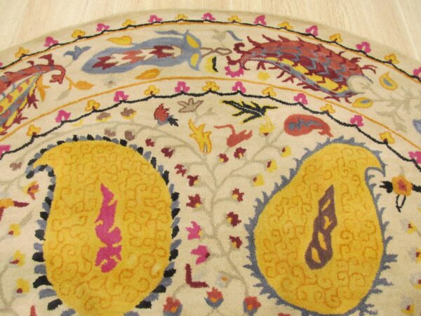 Round rug with yellow paisley and multicolored floral motifs on a cream background near light wood floor.