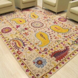 Beige rug featuring bright yellow paisley and multicolor floral designs sits on light wood flooring.