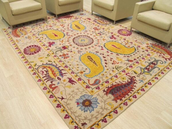 Beige rug featuring bright yellow paisley and multicolor floral designs sits on light wood flooring.