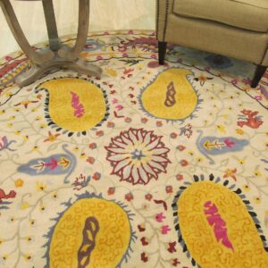 Cream round rug with colorful yellow, pink, and blue floral and paisley patterns next to furniture.
