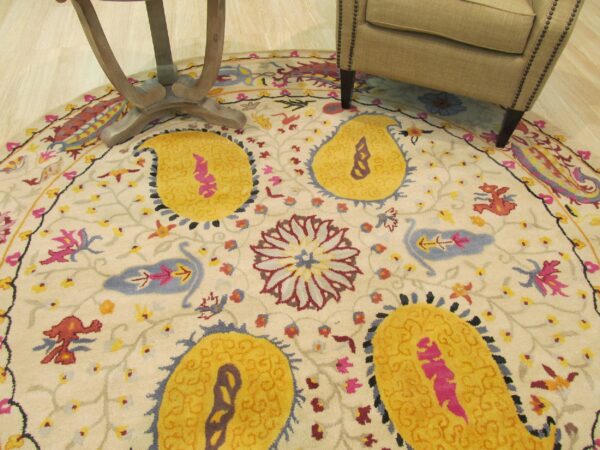 Cream round rug with colorful yellow, pink, and blue floral and paisley patterns next to furniture.