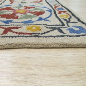 Cream high-pile rug with colorful floral motifs and dark outlines rests on light wood plank flooring.
