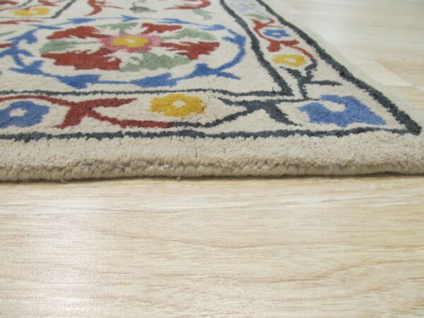Cream high-pile rug with colorful floral motifs and dark outlines rests on light wood plank flooring.