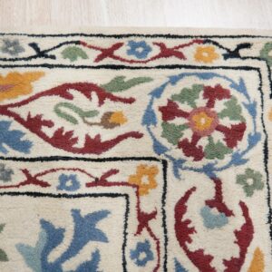 Cream area rug with a dense pile and multi-colored traditional floral border on light wood planks.
