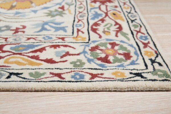 An ivory rug with red, blue, green, and yellow floral borders rests on light wood planks.