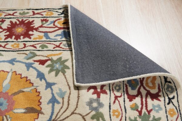 Close-up of a medium-pile, multicolored floral rug laid on light wood flooring, revealing its gray backing.