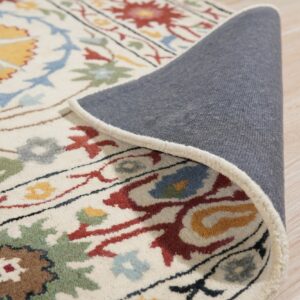 Cream floral rug detail showing multicolored pattern and gray backing, resting on light wood floorboards.