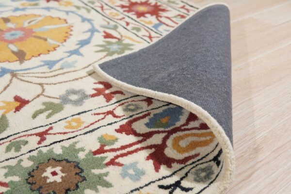 Cream floral rug detail showing multicolored pattern and gray backing, resting on light wood floorboards.