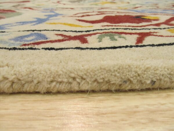 Angled view of a thick-pile cream rug with colorful abstract designs resting on light wood flooring.