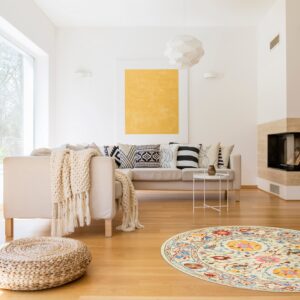 Cream round rug with colorful floral motifs rests on light wood floors in a modern living room.