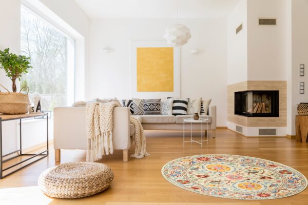 Cream round rug with colorful floral motifs rests on light wood floors in a modern living room.