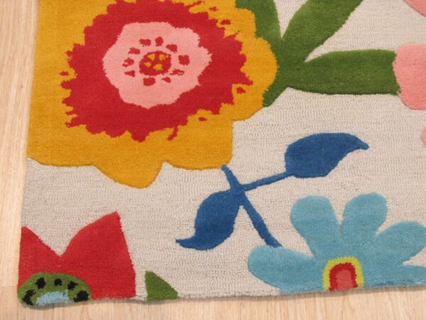 Red, yellow, blue, and green stylized flowers cover this beige loop pile rug shown on wood flooring.