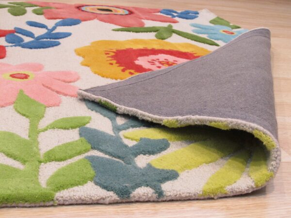 A colorful high-pile floral rug is peeled back, showing the gray backing on light wood flooring.