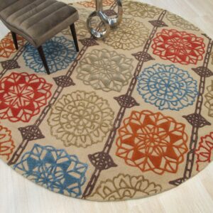 A round, neutral rug with red, blue, green, and orange floral medallions rests on light wood flooring.