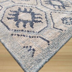 The corner of a textured blue and white rug with geometric patterns rests on light hardwood flooring.