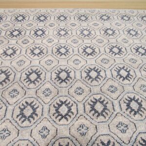 Greige low-pile rug featuring a geometric trellis pattern with dark blue tribal motifs on wood flooring.