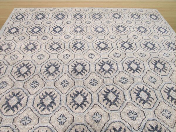 Greige low-pile rug featuring a geometric trellis pattern with dark blue tribal motifs on wood flooring.