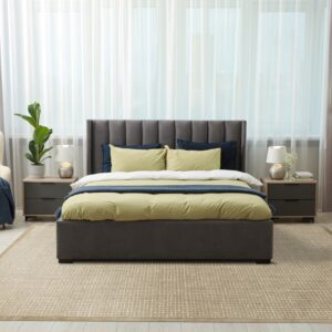 A textured tan rug with a woven grid pattern lies beneath a gray upholstered bed on light wood flooring.