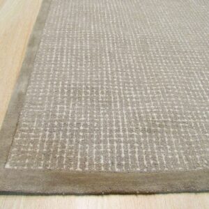 Textured beige rug featuring an irregular grid pattern and a uniform taupe border on light wood floor.