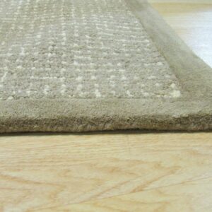 Medium-pile beige rug showing a textured abstract pattern and a smooth border on light wood flooring.