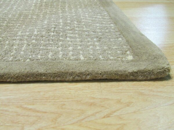 Medium-pile beige rug showing a textured abstract pattern and a smooth border on light wood flooring.