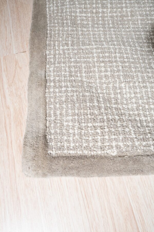 Textured gray and white rug corner with a soft taupe border resting on light wood plank flooring.