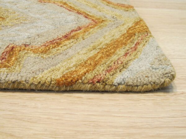 Looped pile rug edge in beige, golden yellow, and reddish-orange zig-zags rests on light wood floor.