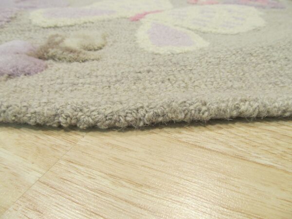 Textured beige area rug with dimensional pink and lavender designs rests on light wood planks.