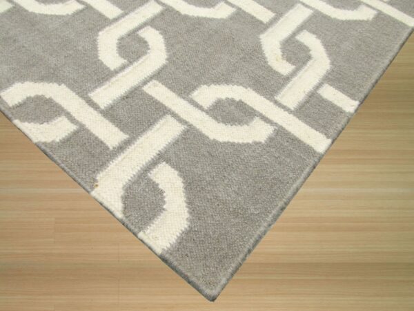 Gray rug with an off-white interlocking geometric pattern lays on light colored wood floor.