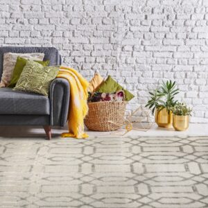 Beige rug with a gray geometric pattern is placed below a gray sofa against a white brick wall.