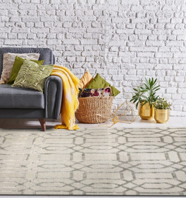Beige rug with a gray geometric pattern is placed below a gray sofa against a white brick wall.
