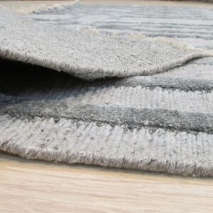 Close-up of a textured gray striped rug with a folded edge lying on light wood flooring.
