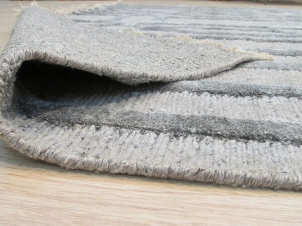 Close-up of a textured gray striped rug with a folded edge lying on light wood flooring.