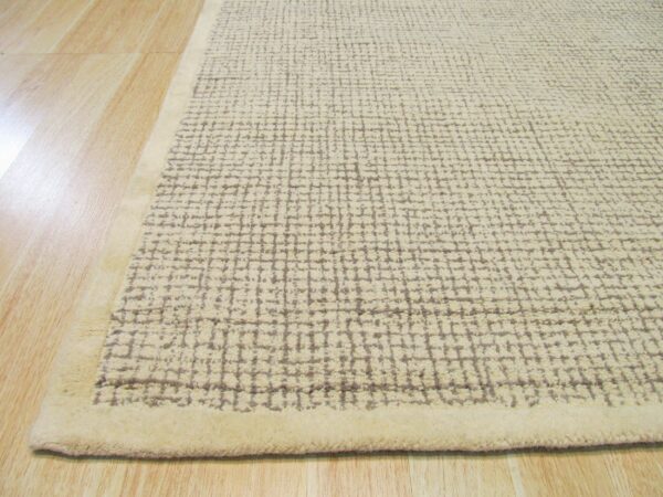 Textured beige rug with a chunky gray grid pattern and solid border sits on light wood planks.