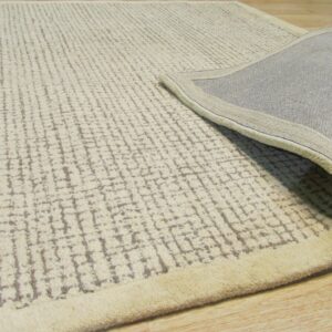 Cream high-pile rug with gray distressed linear patterns, folded over to expose the gray woven backing on a wood floor.