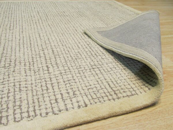 Cream high-pile rug with gray distressed linear patterns, folded over to expose the gray woven backing on a wood floor.