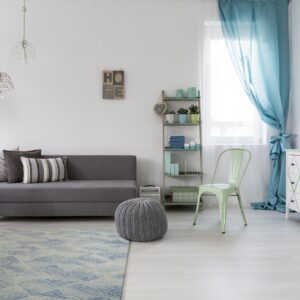 Blue and light gray geometric rug under a gray sofa and knit pouf on light wood floors.