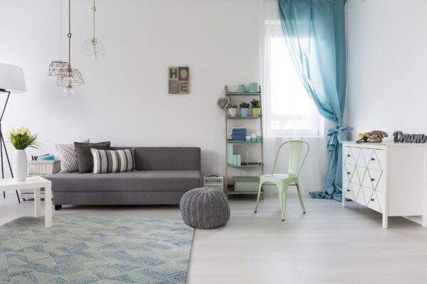 Blue and light gray geometric rug under a gray sofa and knit pouf on light wood floors.